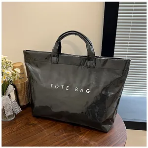 Dettaglio della borsa tote nera lucida in PVC con scritta TOTE BAG bianca su legno