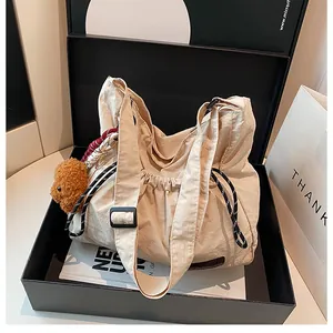 Détail du sac bandoulière en nylon crème avec cordon de serrage et breloque ours