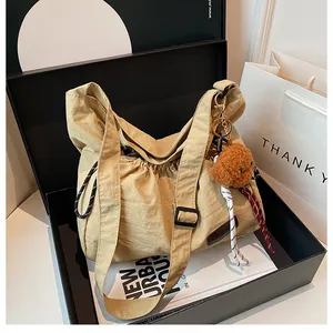 Détail du sac à bandoulière en nylon beige avec cordon et porte-clé ours en peluche