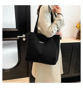 Détail du grand sac cabas noir en daim minimaliste avec une étiquette fashion blanche cousue