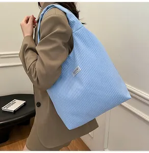 Detail of light blue corduroy tote bag featuring vertical quilting and a white fashion label