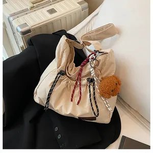 Détail du sac à bandoulière en nylon beige avec cordon de serrage et pendentif ours
