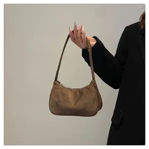 Detail van een bruine suède hobo-tas met een gladde halfronde vorm en zilveren ritssluiting