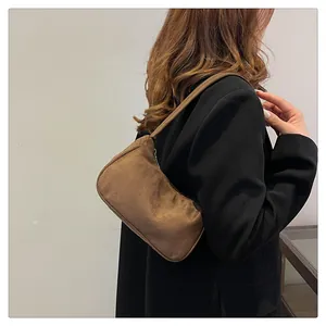 Bruine suède schoudertas in retro baguette-stijl getoond door een fotomodel