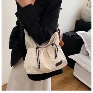 Détail du sac à bandoulière avec cordon, texture nylon blanc cassé et étiquette en cuir
