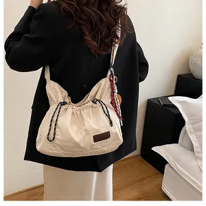Détail de la fermeture à cordon et de l'écusson en cuir sur le sac bandoulière beige