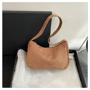 Detailopname bruine suède schoudertas met ritssluiting in minimalistische doos