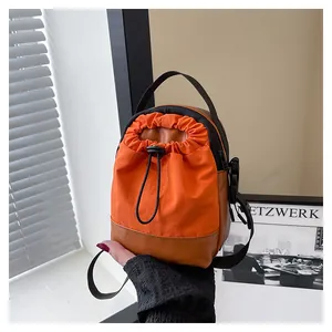 Detail of orange nylon mini crossbody bag showing drawstring closure and synthetic leather base