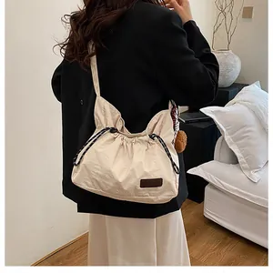 Détail de la fermeture par cordon et de l'écusson sur le sac à bandoulière en nylon beige