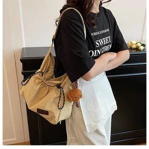 Détail du sac à bandoulière kaki avec cordon, breloque ours et écusson de mode