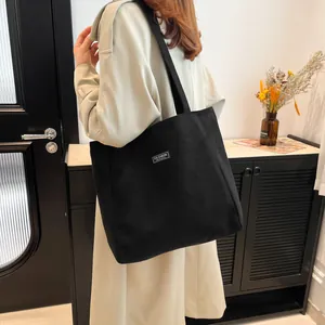 Sac fourre-tout minimaliste en velours côtelé noir porté par une femme sur l'épaule