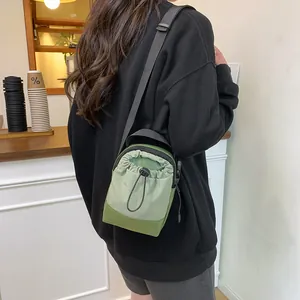 Green nylon crossbody bag with drawstring closure worn by model in cafe setting
