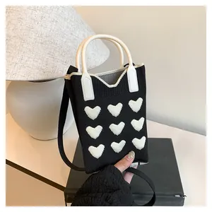 Detail of a mini knitted black heart tote bag with white leather handle and strap