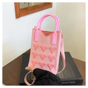 Detail of pink knitted bag featuring 3D heart embossments on a wooden table surface