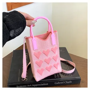 Detail of pink knitted mini bag with 3D heart patterns on a stylish book background