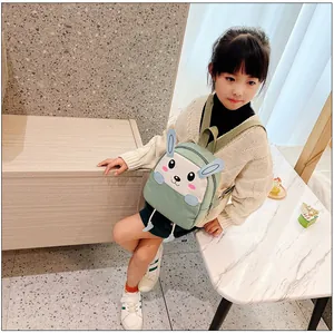 Détail d'un sac à dos lapin vert en toile avec oreilles 3D porté par un enfant en intérieur