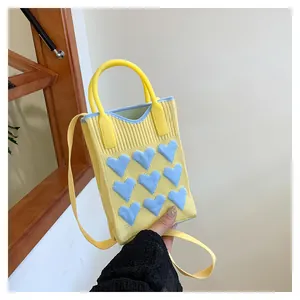 Detail shot of yellow knitted mini bag with blue 3D heart patterns and carrying handle