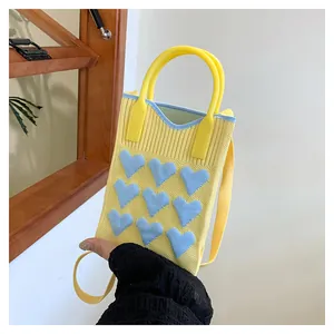 Detail of yellow knitted mini bag featuring blue 3D heart motifs and texture