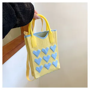 Close-up of yellow knit mini bag featuring 3D light blue heart patterns and textured fabric