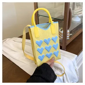 Detailed knit texture of a yellow mini bag with soft blue 3D heart-shaped patches