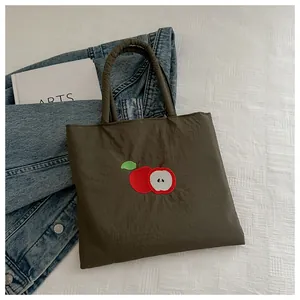 Detail of dark brown canvas tote bag featuring premium red apple embroidery patterns