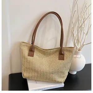 Dettaglio della borsa tote in paglia intrecciata con tracolle in pelle marrone e cuciture a croce