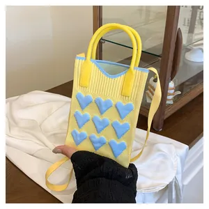 Close-up of a yellow knitted mini phone bag with blue heart patterns on silk fabric