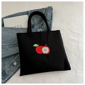 Detail of black canvas tote bag featuring a high-quality red and green apple embroidery