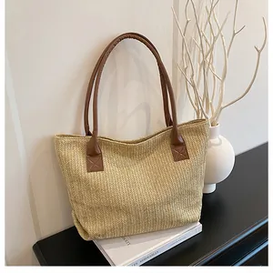 Dettaglio borsa tote in paglia intrecciata con manici in pelle marrone su tavolo nero