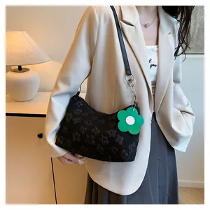 Detail of black floral embossed canvas tote bag with a green flower charm and metal chain