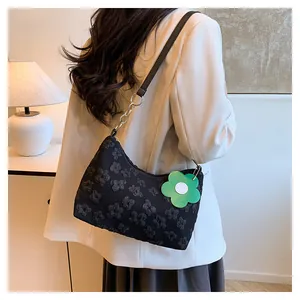 Detail of black floral textured shoulder bag with green flower charm and metal chain