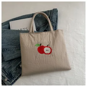 Detail of beige canvas tote bag featuring vibrant red apple embroidery and top handles