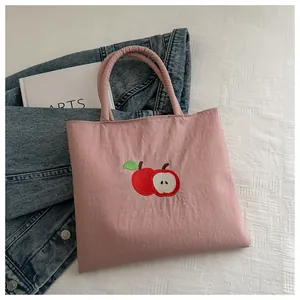 Detailed embroidery of red apples on a pink canvas tote bag with tubular handles