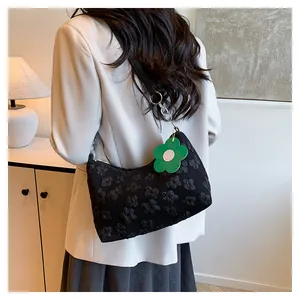 Detail of black floral textured hobo bag with a green flower charm and metal buckle