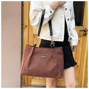 Detail of brown corduroy tote bag showing vertical texture and gold chain strap accents