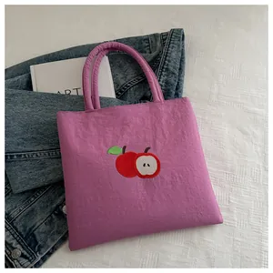 Detail of red apple embroidery on a vibrant purple canvas tote bag for casual style