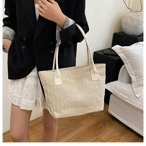 Dettaglio della borsa tote in paglia con manici in finta pelle beige indossata da modella