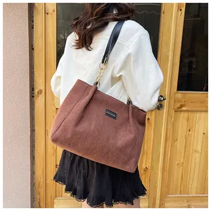 Detail of brown corduroy tote bag showing metal chain strap and fashion label on front