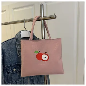 Detail of pink canvas tote bag featuring a cute red apple embroidery on a textured fabric