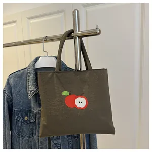 Detail of olive green canvas tote bag featuring embroidered red apple design and texture