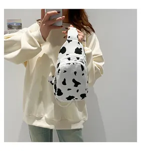 Detail of cow print canvas chest bag featuring dual zippers and adjustable white strap