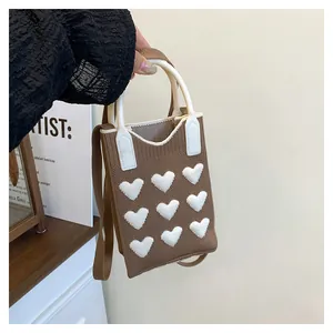 Detail of brown knitted mini handbag with 3D white hearts and rounded top handle