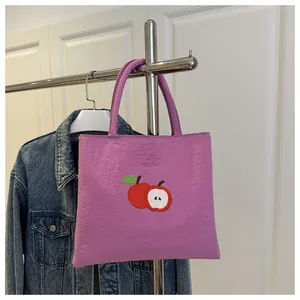 Detail of purple canvas tote bag with embroidered apple design hanging on a metal rack