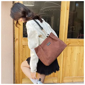 Detail of brown corduroy tote bag featuring leather chain strap and fashion label on shoulder