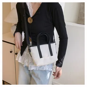 Gros plan d'un mini sac bandoulière en toile blanc cassé avec lanières noires sur un mannequin