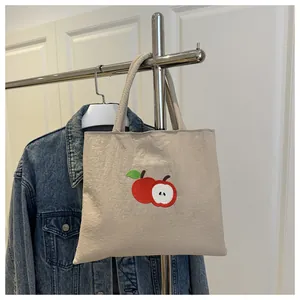 Detail of beige canvas tote bag with red apple embroidery on a silver metal hanger