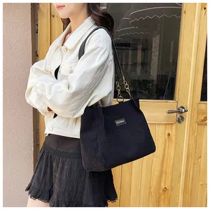 Detail of fashion black corduroy tote bag showing metal chain strap and luxury logo label
