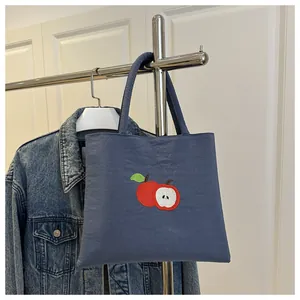 Detailed red apple embroidery on a dark blue canvas tote bag hung on a metal hook