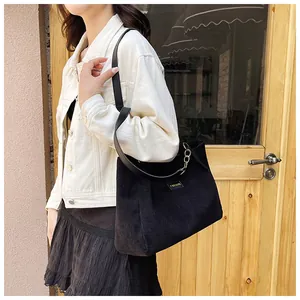 Detail of black corduroy tote bag featuring leather shoulder strap and gold chain link
