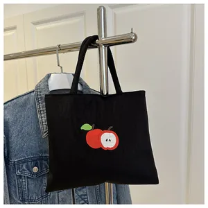 Detail of embroidered apple pattern on black canvas tote bag hanging on a hanger